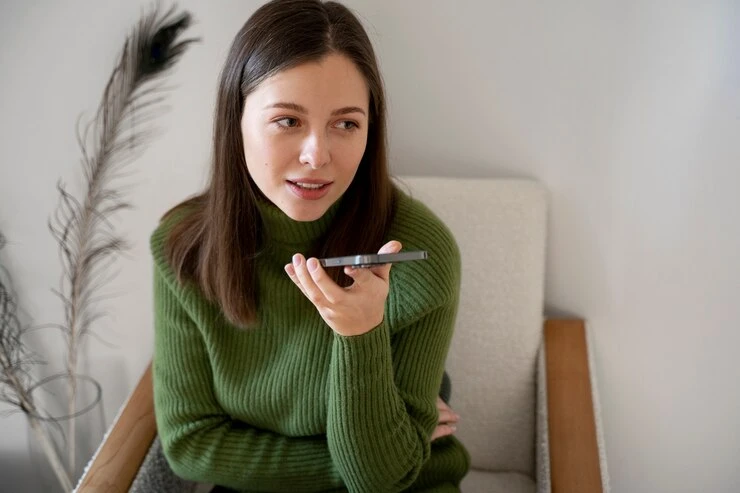 Mulher usando busca por voz em um smartphone enquanto senta em uma cadeira. A imagem explora o conceito de SEO e tecnologias de voz.