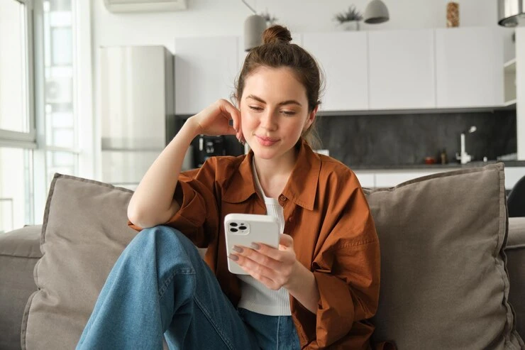 Mulher utilizando smartphone com foco em pesquisa por voz, sentada em sofá em ambiente moderno e aconchegante, evidenciando a tecnologia e a interação.