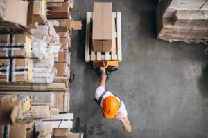 Funcionário mancheando uma caixa sobre um rolete de carga em depósito de logística, destaque para o uso do rolete na movimentação de cargas internas.